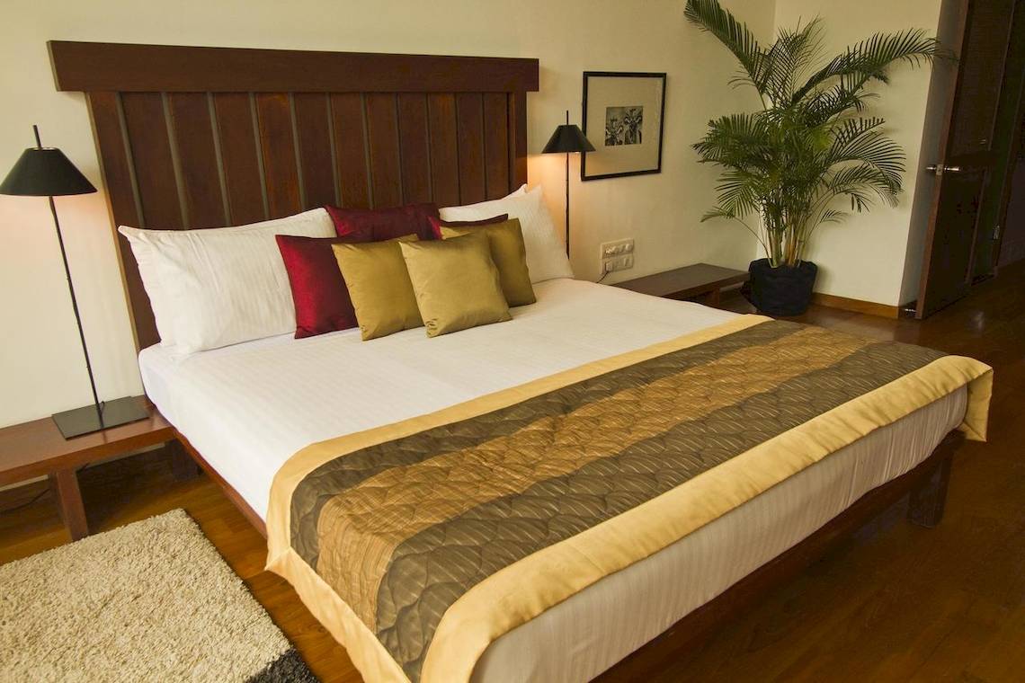 Hotelzimmer mit Bett, Kissen, Nachttischen und Pflanzen.