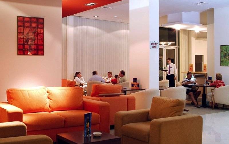 Lobby des Festa Panorama Hotels mit orangefarbenen Sofas, Gästen und einem Barbereich.