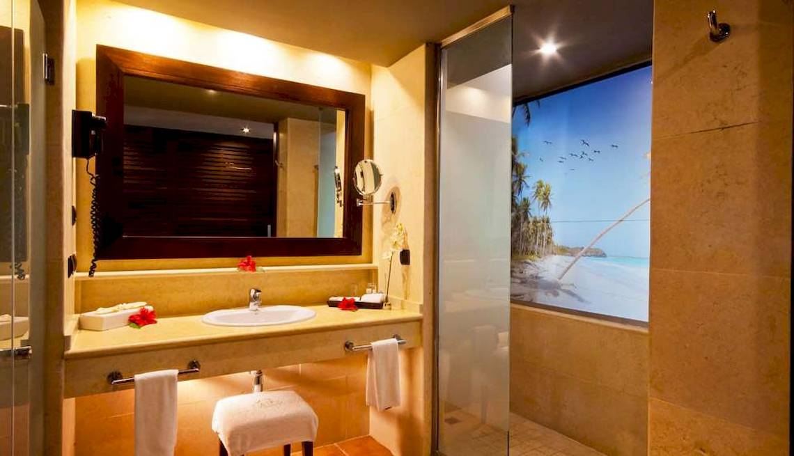 Badezimmer mit Spiegel, Waschbecken und Glasdusche, Blick auf den Strand.