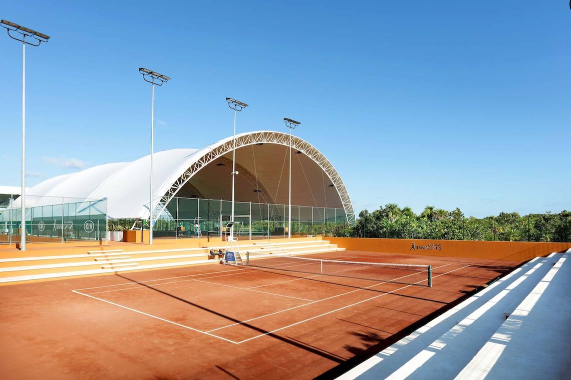 Tennisanlage im Grand Palladium Costa Mujeres Resort & Spa mit blauem Himmel und orangefarbenen Wänden.