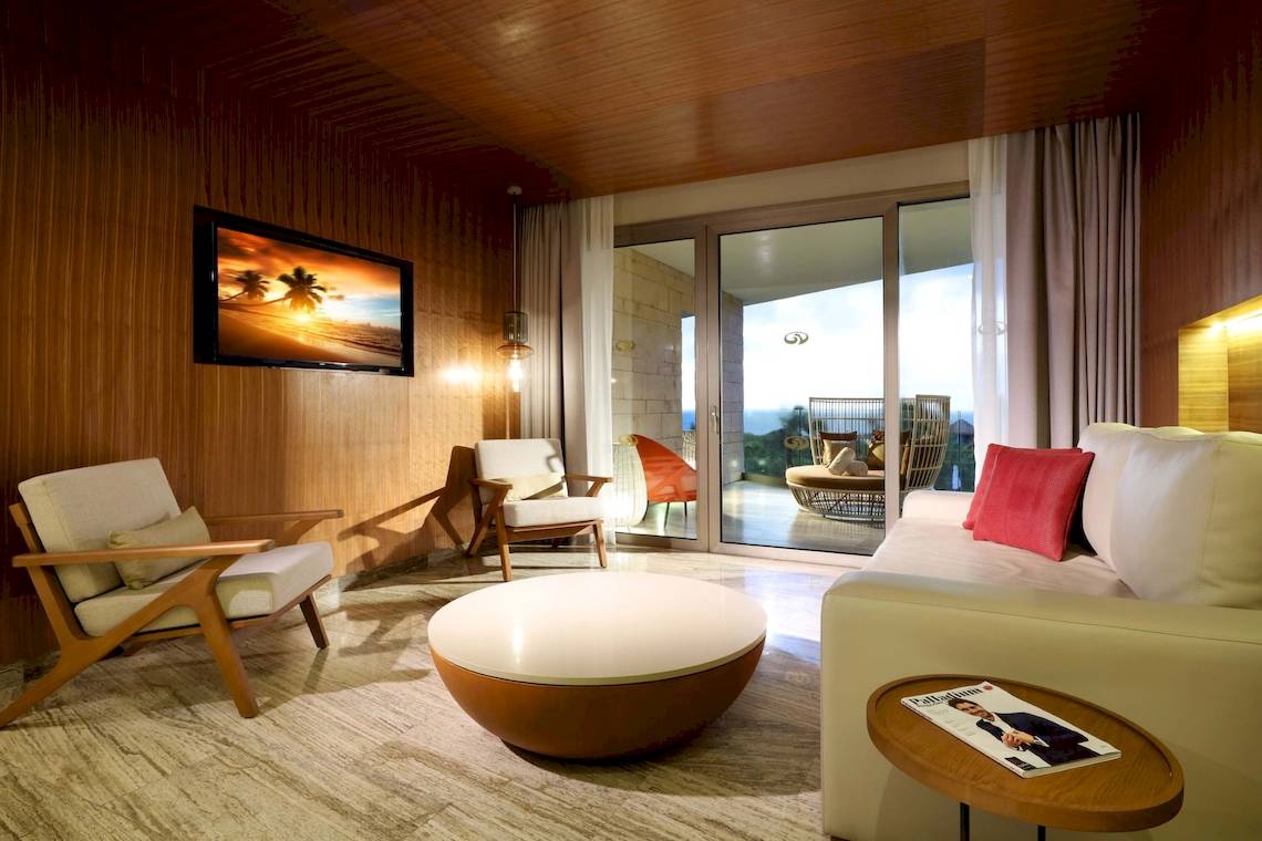 Innenansicht einer Suite im Grand Palladium Costa Mujeres Resort & Spa mit Wohnzimmer, Fernseher, und Balkon.