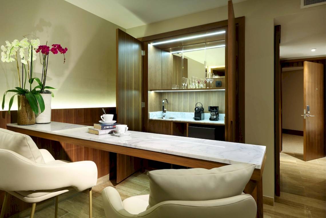 Suite-Wohnbereich im Grand Palladium Costa Mujeres Resort & Spa mit weißem Marmortisch, Sesseln und Blumenvase.