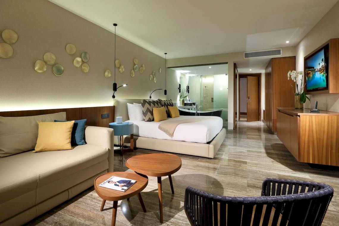 Schlafzimmer im Grand Palladium Costa Mujeres Resort & Spa mit einem großen Bett, einem Wohnzimmerbereich und einer modernen Einrichtung.