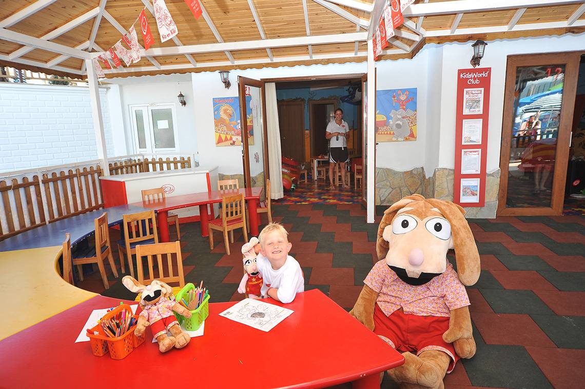 Ein Kind sitzt im Eftalia Aqua Resort Kids Club Raum mit Puppen und Zeichenmaterial.