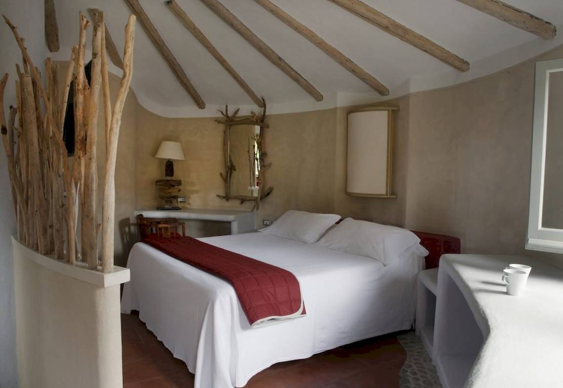 Schlafzimmer im Baia del Sole Hotel mit einem Bett, weißen Laken, einem roten Quilt und Holzelementen an der Wand.