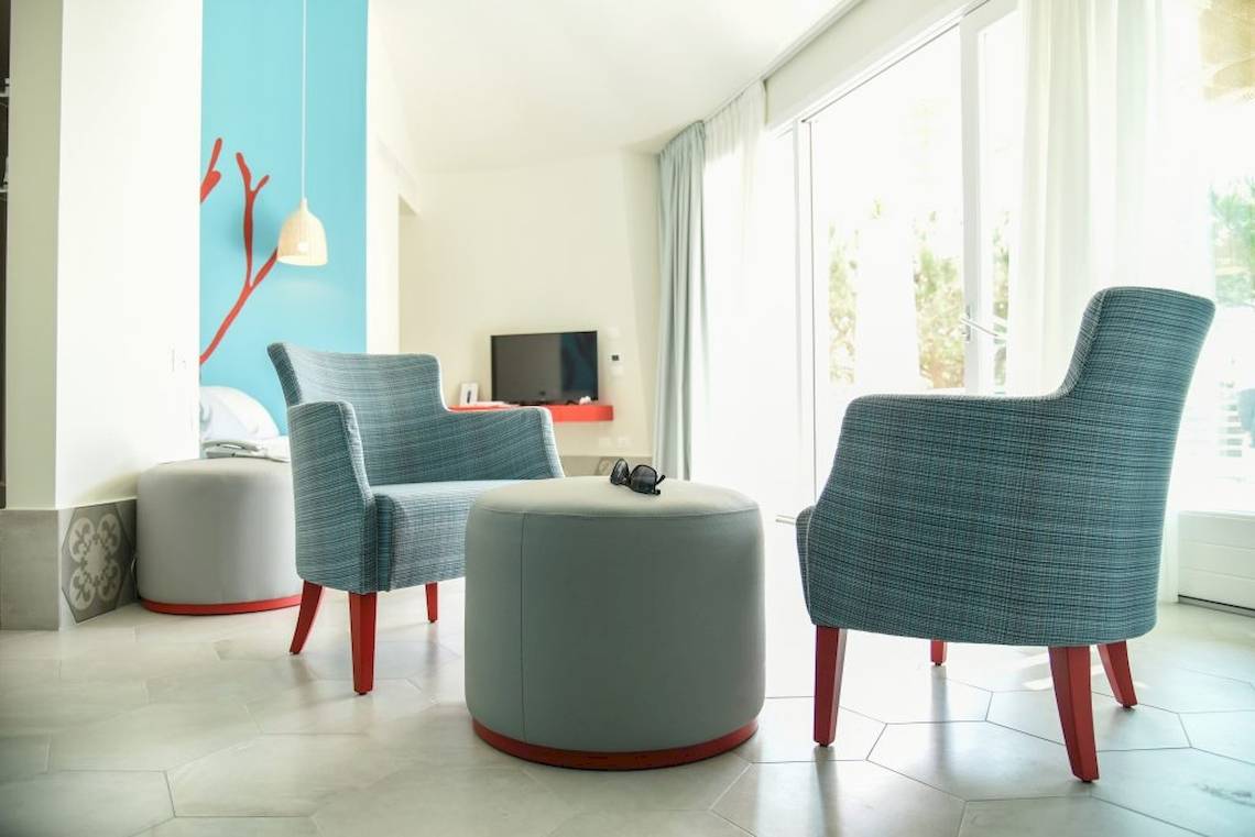 Wohnbereich des Baia del Sole Hotels mit zwei blauen Stühlen, einem Tisch und einem Fernseher.