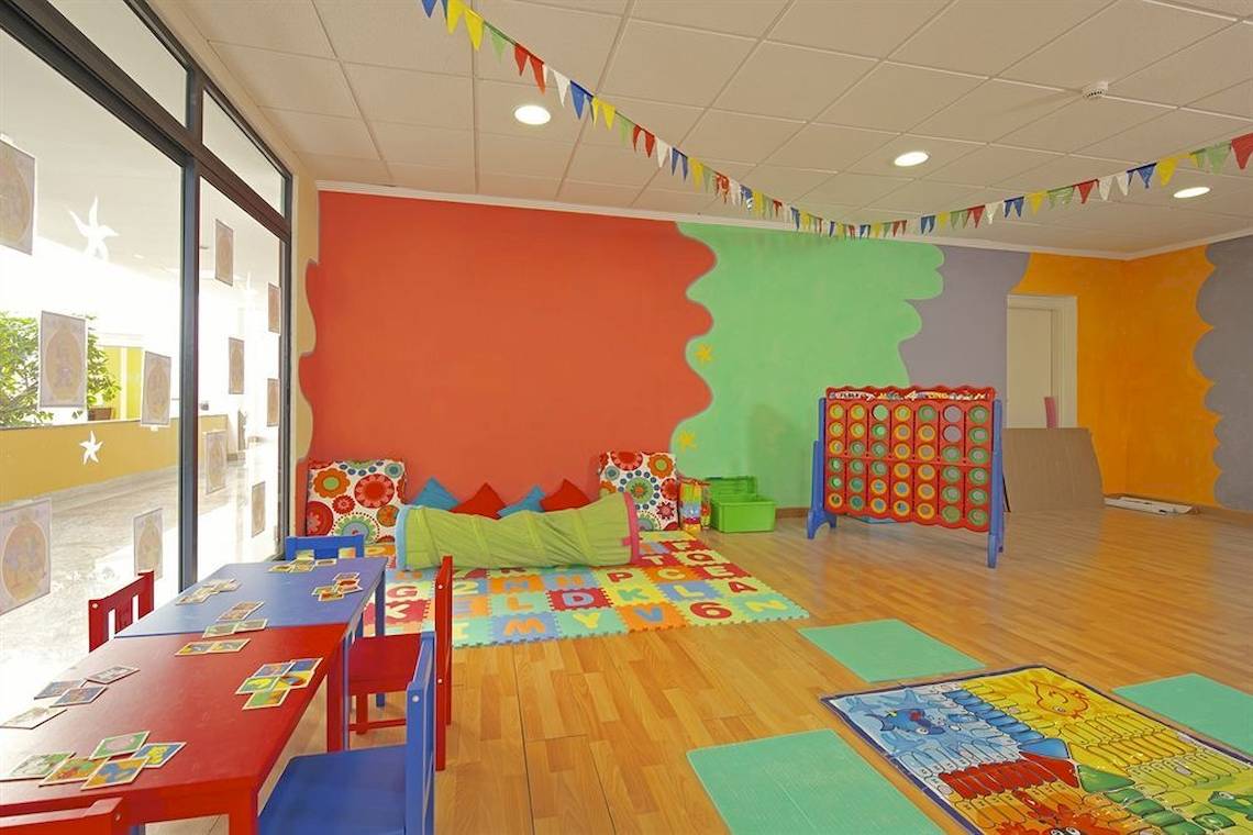 Kinderspielzimmer im Mirador Papagayo by LIVVO mit bunten Wänden, Tisch, Stühlen und Spielzeug.