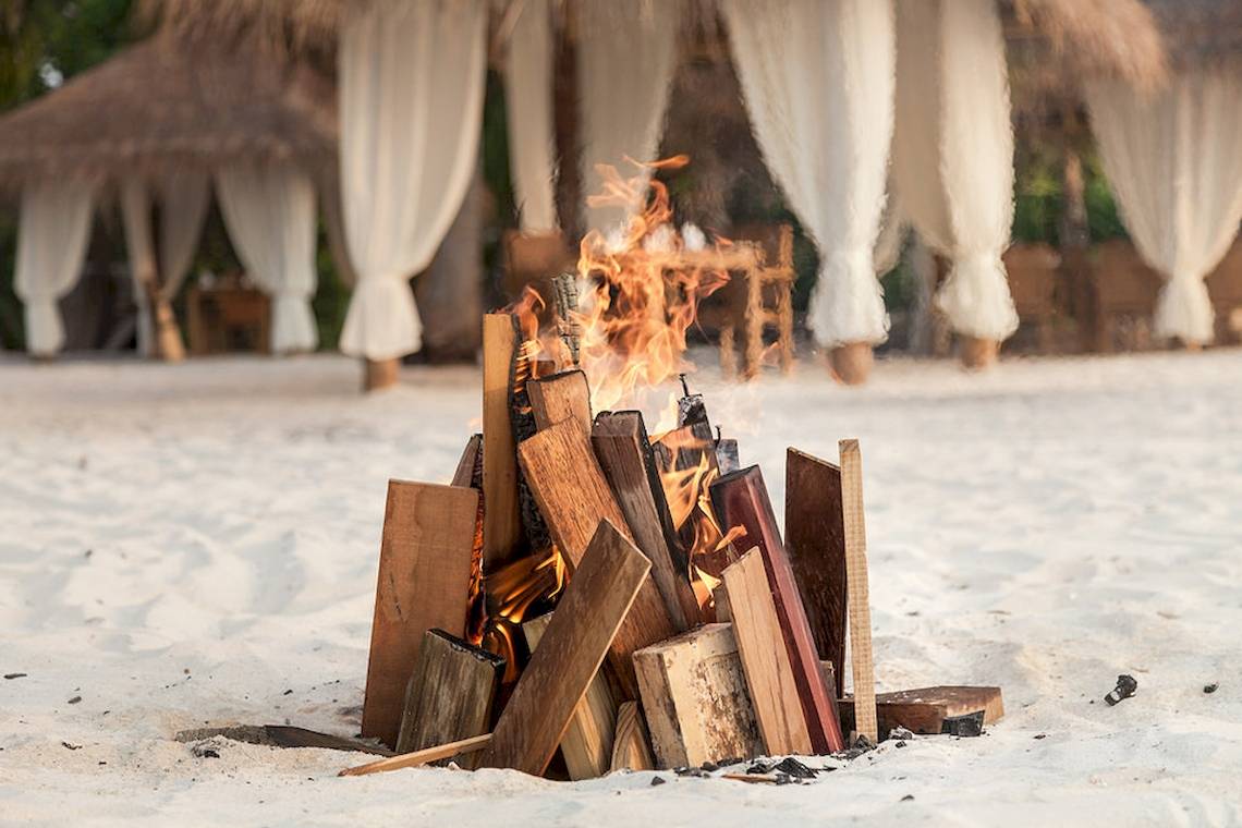 Feuerstelle auf dem Strand mit Holz und Flammen vor einem Pavillon