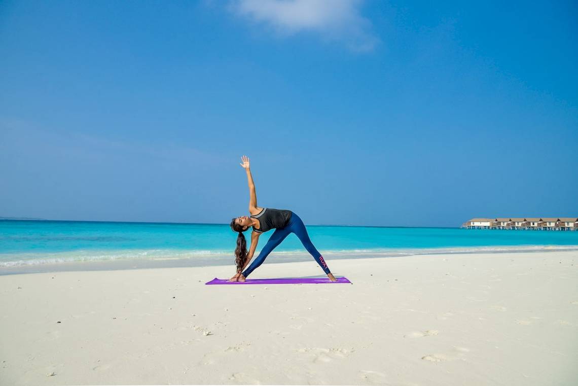 Eine Frau praktiziert Yoga auf dem Strand im Reethi Faru Resort.