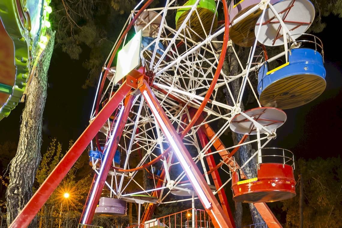 Ein nachts beleuchtetes Riesenrad im Freizeitpark mit verschiedenen farbigen Gondeln.