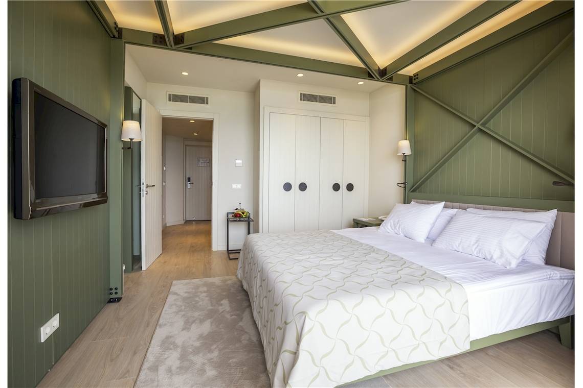Schlafzimmer im Voyage Sorgun Hotel mit einem Doppelbett, Fernseher an der Wand und grünen Wänden.