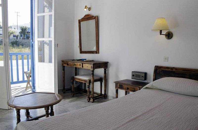 Ein Schlafzimmer mit Balkon und Holzmöbeln, einschließlich eines Bettes, eines Schreibtisches und eines Spiegels.