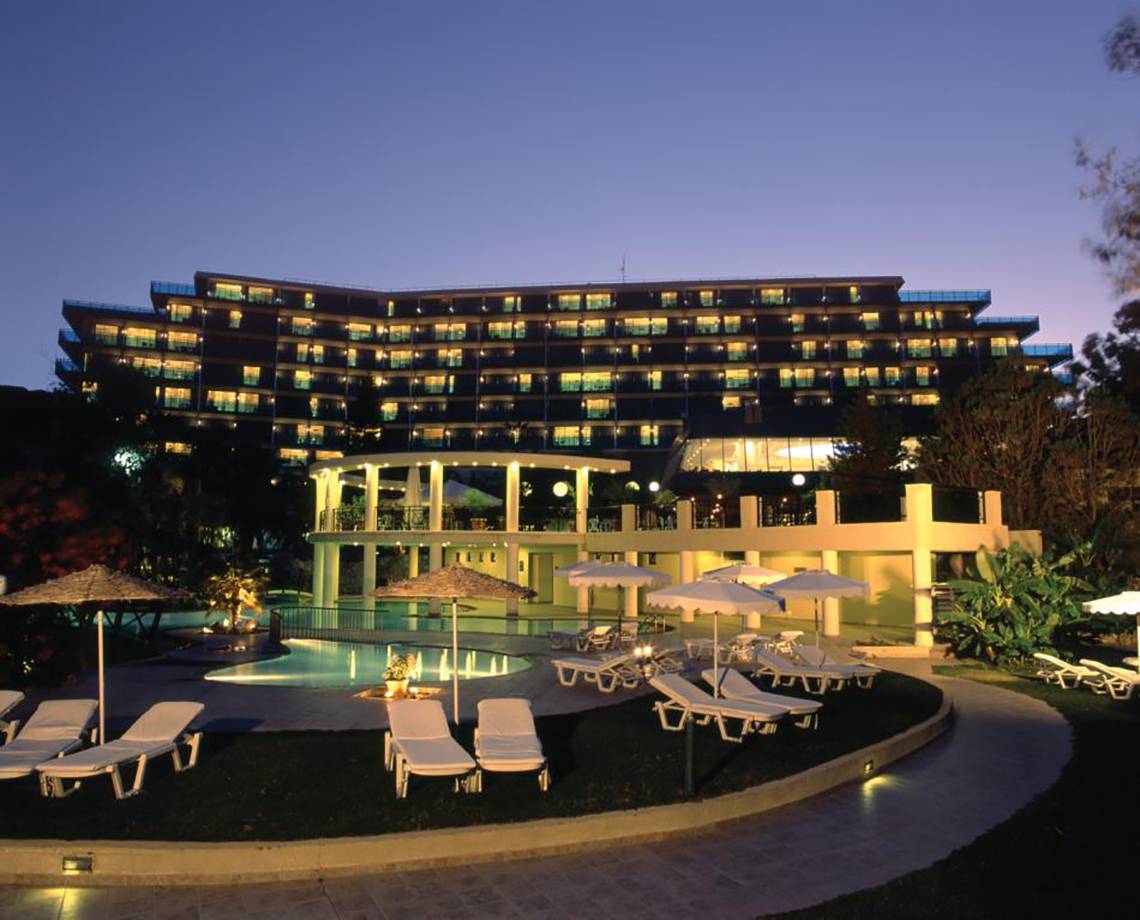Abendliche Ansicht des Calypso Beach Hotels mit illuminierten Fenstern und Außenbereich mit Pool und Liegestühlen.