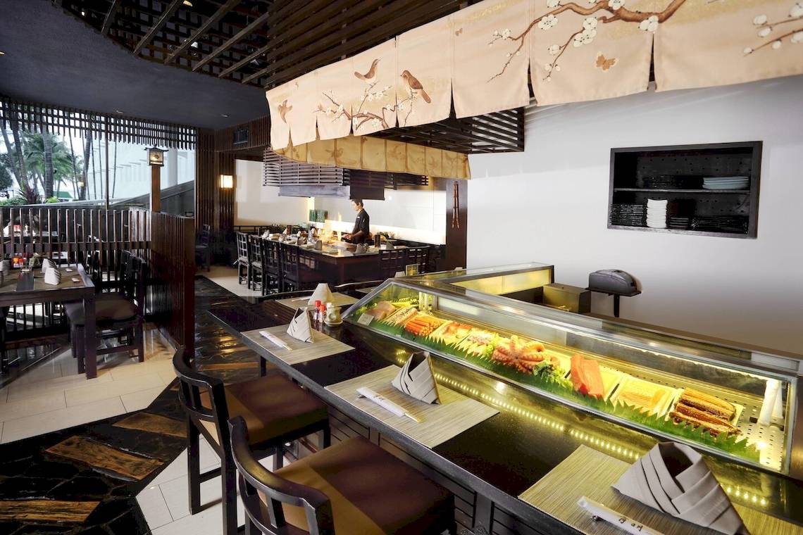 Innenansicht des Restaurants im Le Meridien Phuket Beach Resort mit Sushi-Bar und Tischen.