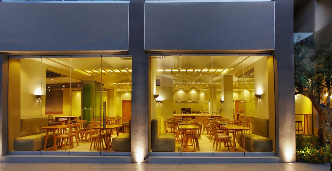 Außenansicht des Anna's House Restaurants mit großen Glasfenstern und innenliegenden Holztischen und Stühlen.