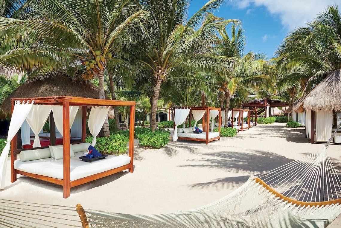 Strandbetten im El Dorado Royale Spa Resort mit weißen Vorhängen und blauen Handtüchern.