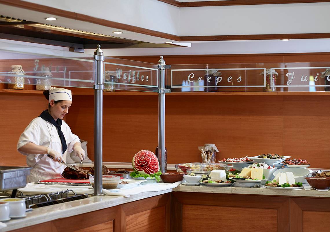 Buffettisch im Serita Beach Hotel mit verschiedenen Gerichten und einer Frau, die serviert.