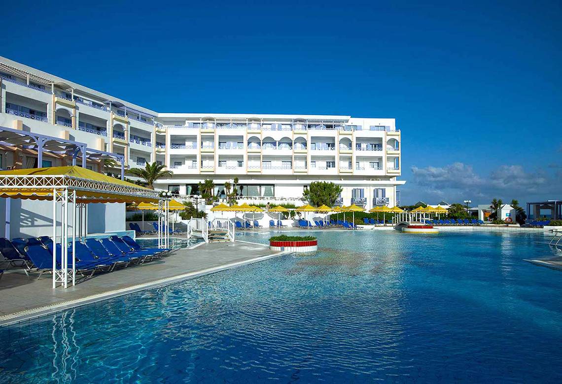 Außenpool des Serita Beach Hotels mit blauen Sonnenliegen und gelben Sonnenschirmen.