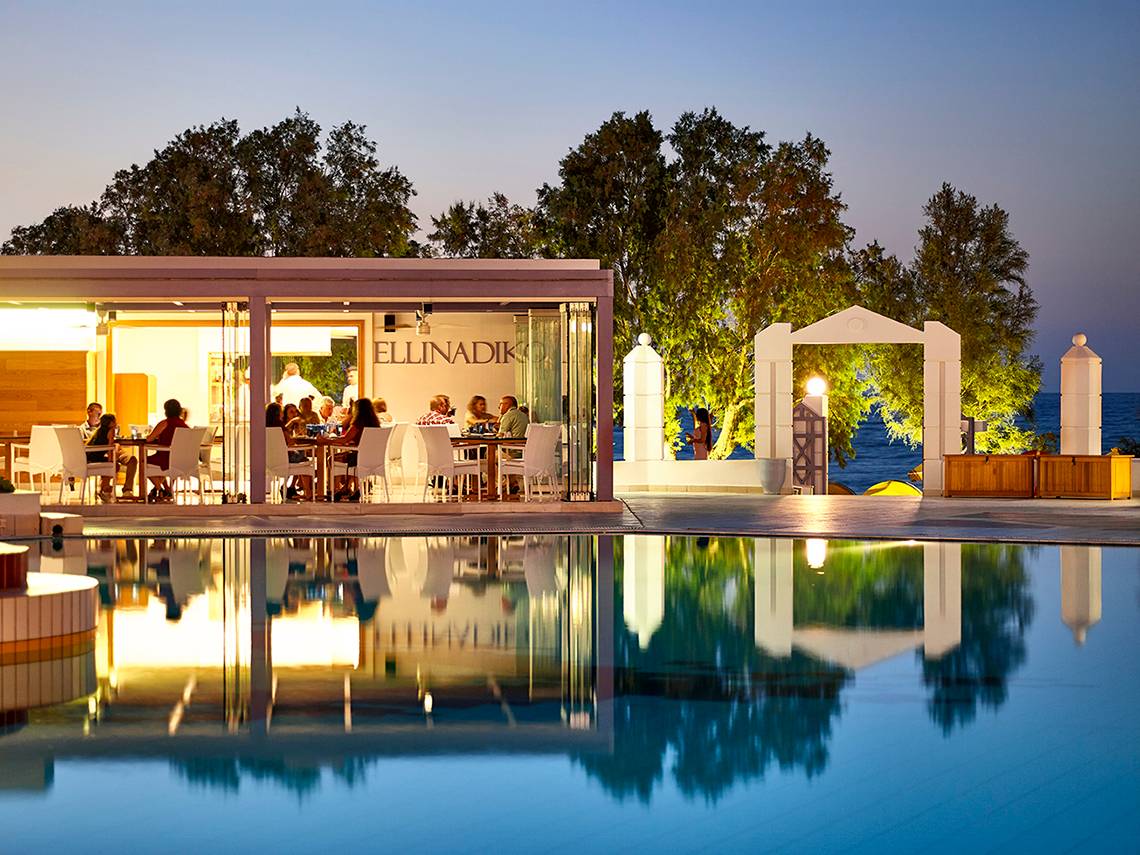 Abendansicht der Poolterrasse im Serita Beach Hotel mit Gästen und Blick auf das Meer.