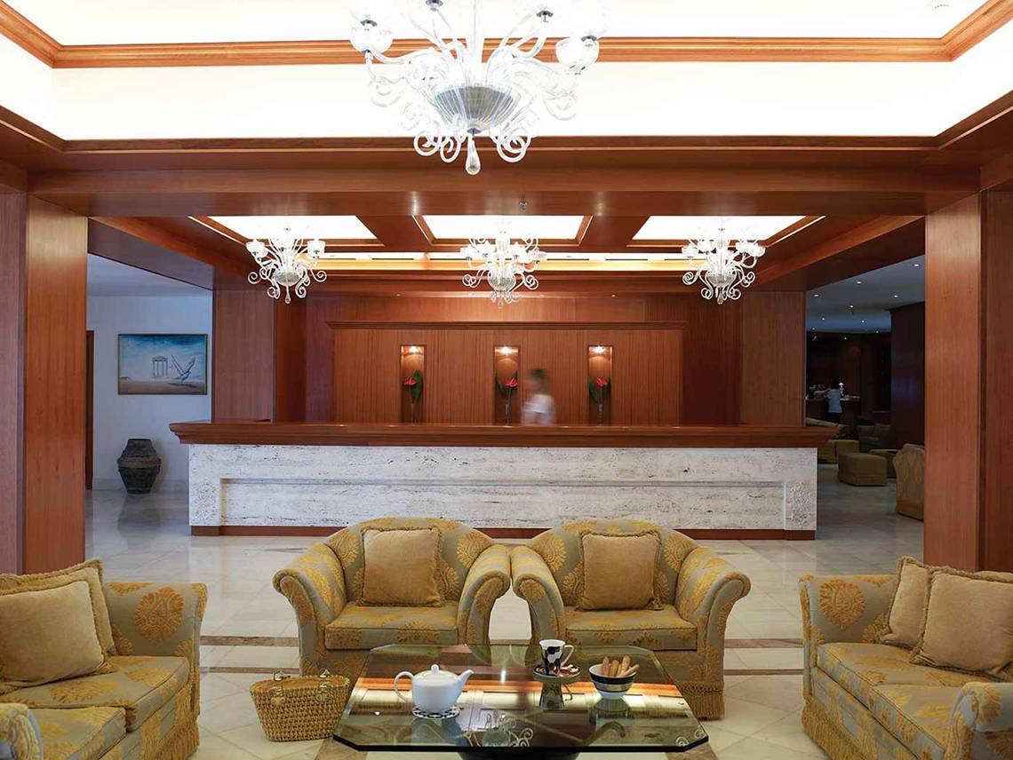 Hotellobby des Serita Beach mit goldenen Möbeln, Kronleuchtern und einem Empfangstresen.