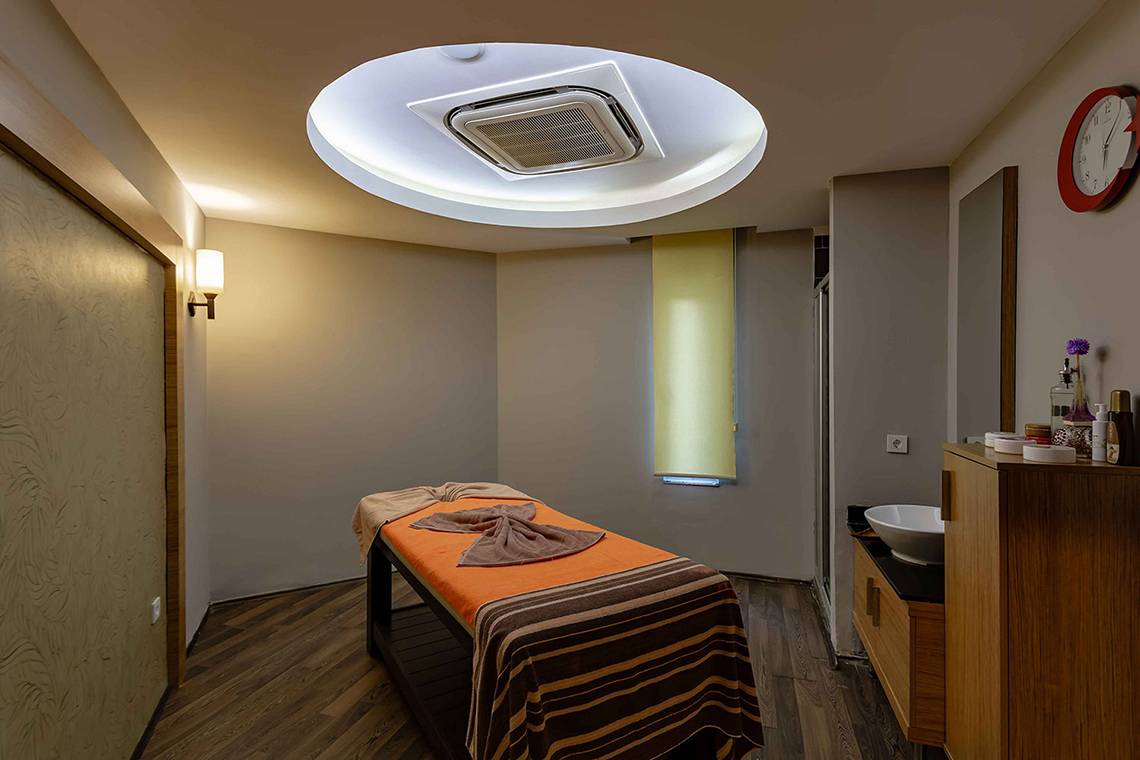 Massageraum im Asteria Family Resort Side mit einem Behandlungstisch, einer Lampe und einer Uhr.