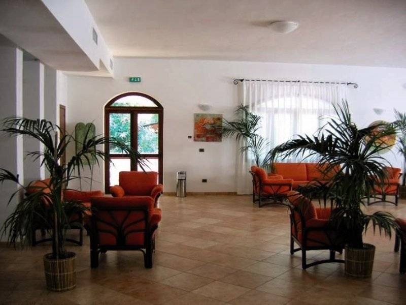 Hotellobby von Gabbiano Beach Vieste mit roten Sesseln, Pflanzen und einer Couch.