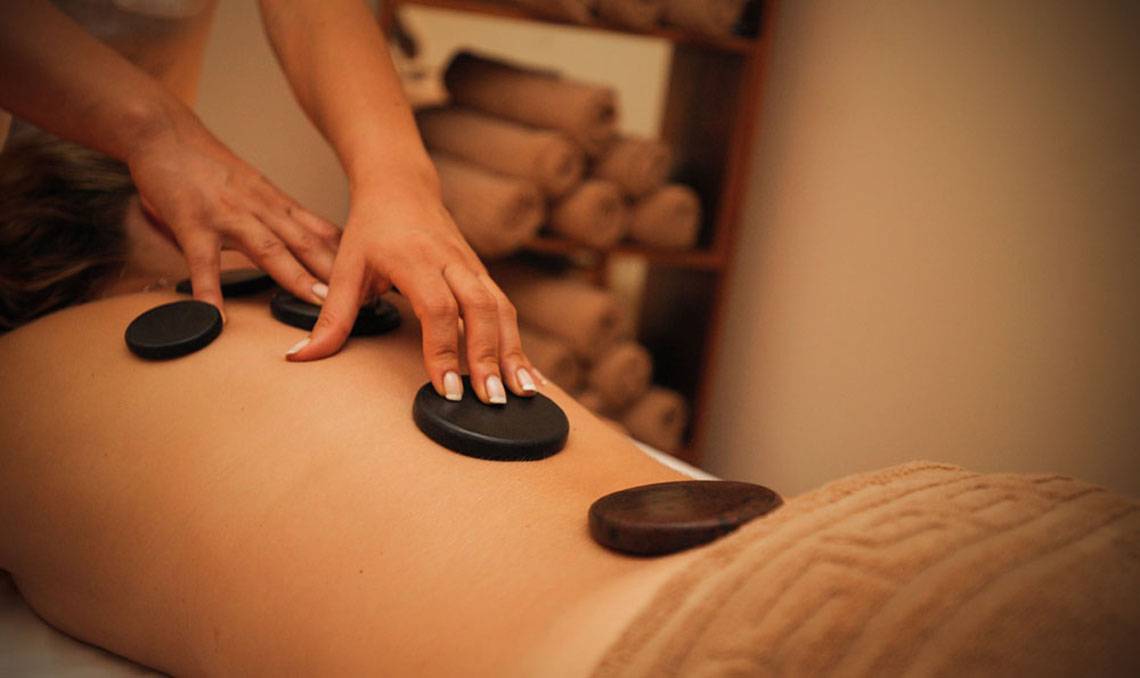 Massagebehandlung im Grand Belish Resort Hotel & Spa mit schwarzen Steinen auf dem Rücken einer Person.