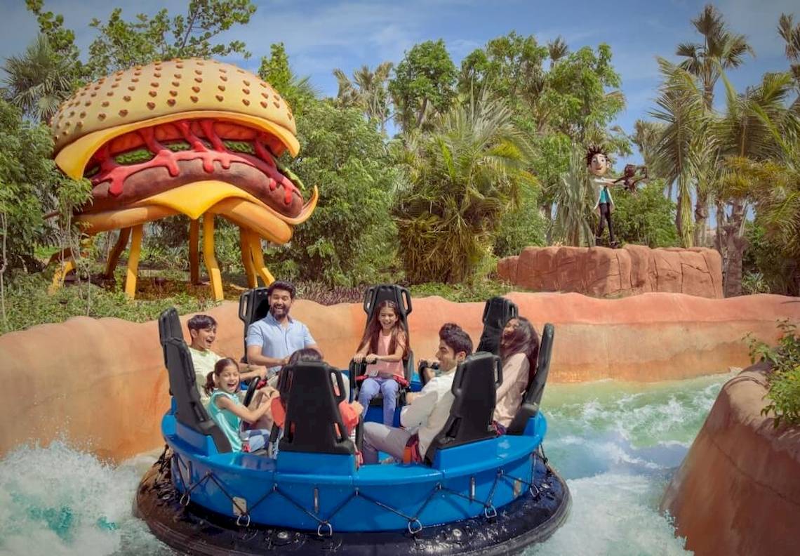 Familie im Ja Lake View Hotel auf einer blauen Wasserrutsche, mit einem riesigen Hamburger im Hintergrund.