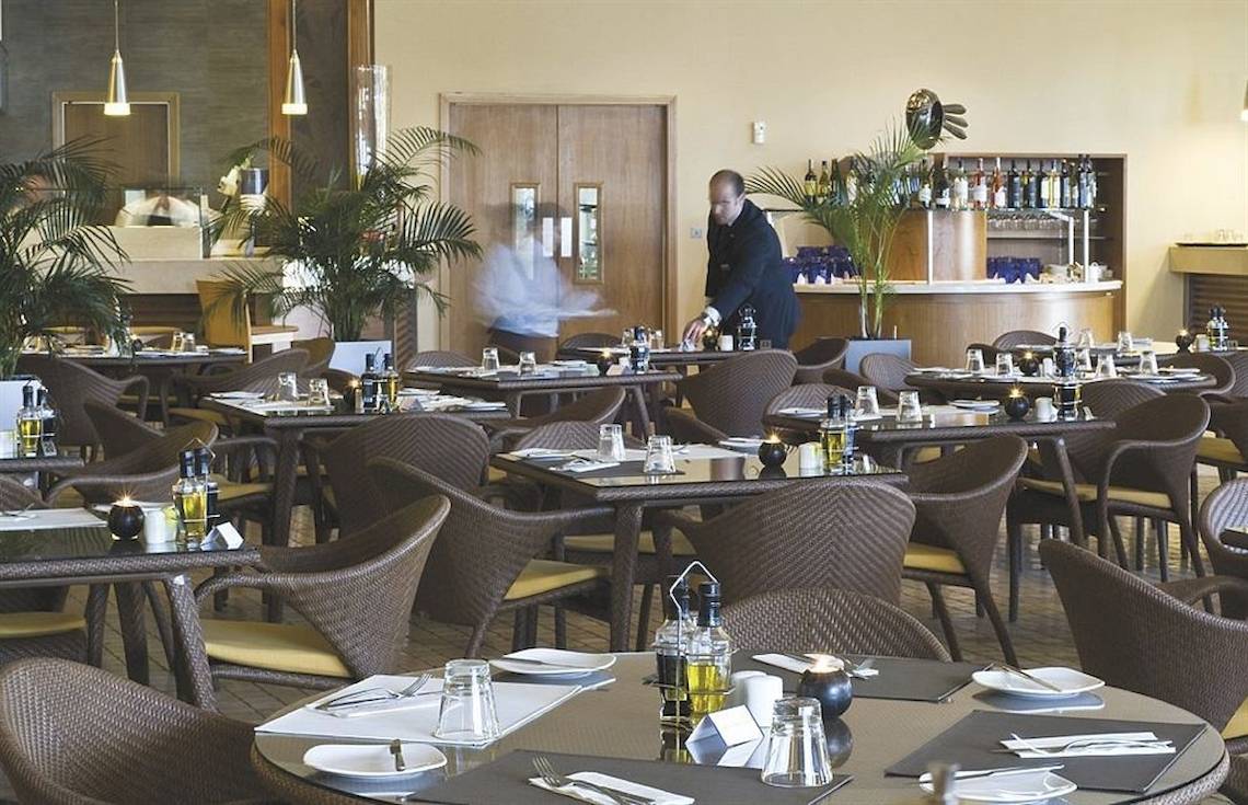 Restaurant im Radisson Blu Resort & Spa, Malta Golden Sands mit gedeckten Tischen und einem Kellner.