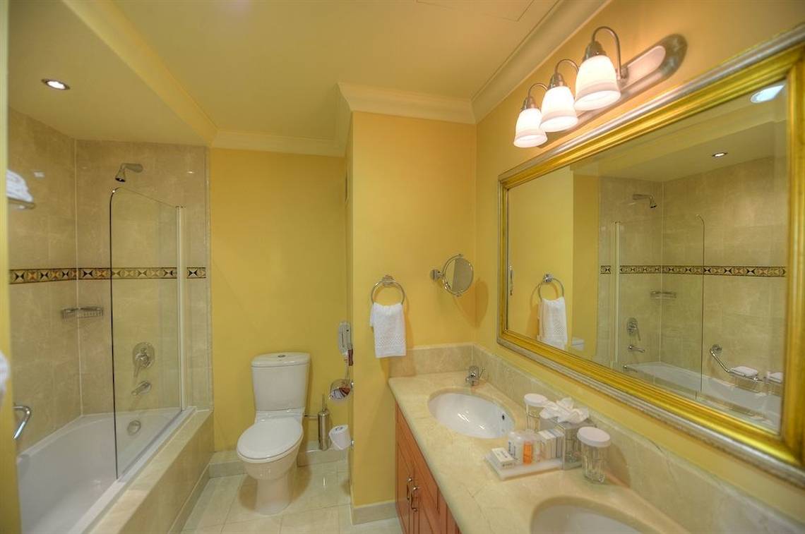 Badezimmer im Radisson Blu Resort & Spa, Malta Golden Sands mit gelben Wänden, einer Badewanne und einer Dusche.