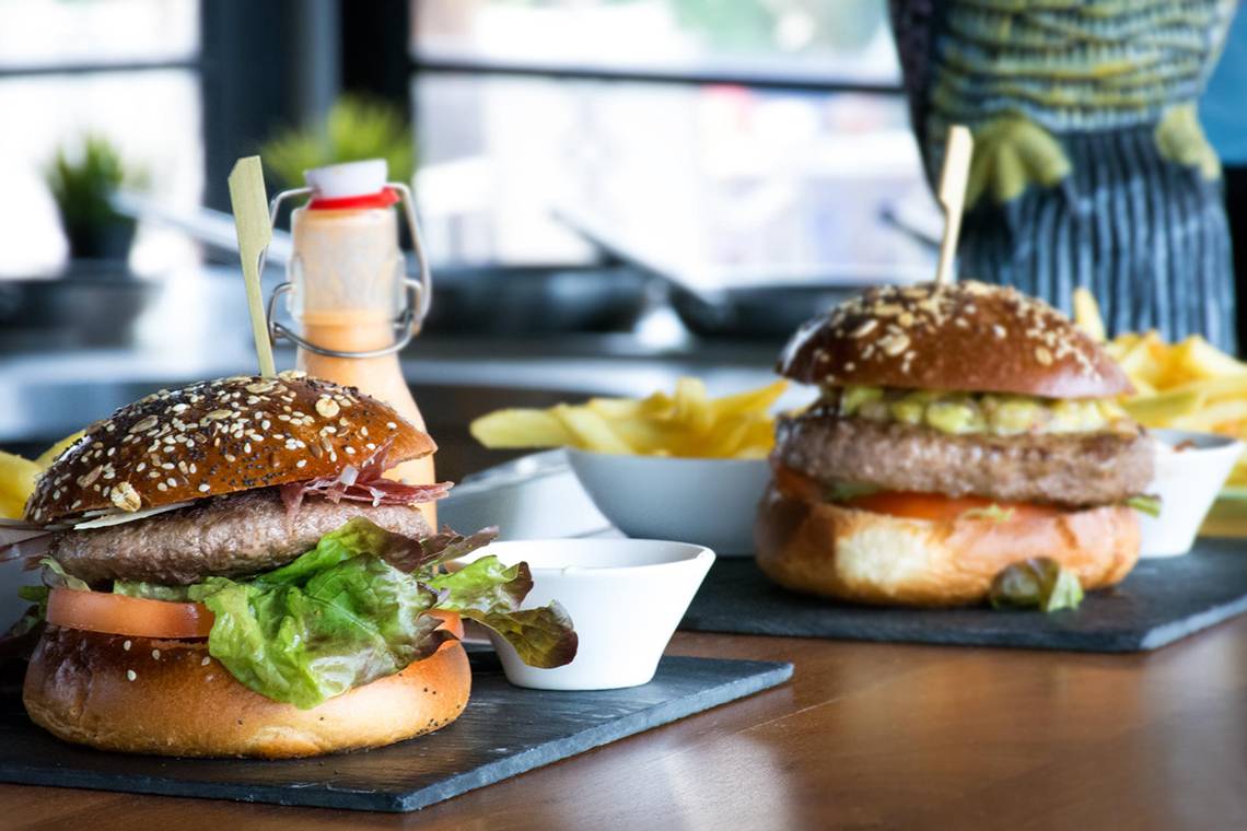 Zwei Burger auf einem Tisch mit Pommes und Saucen.