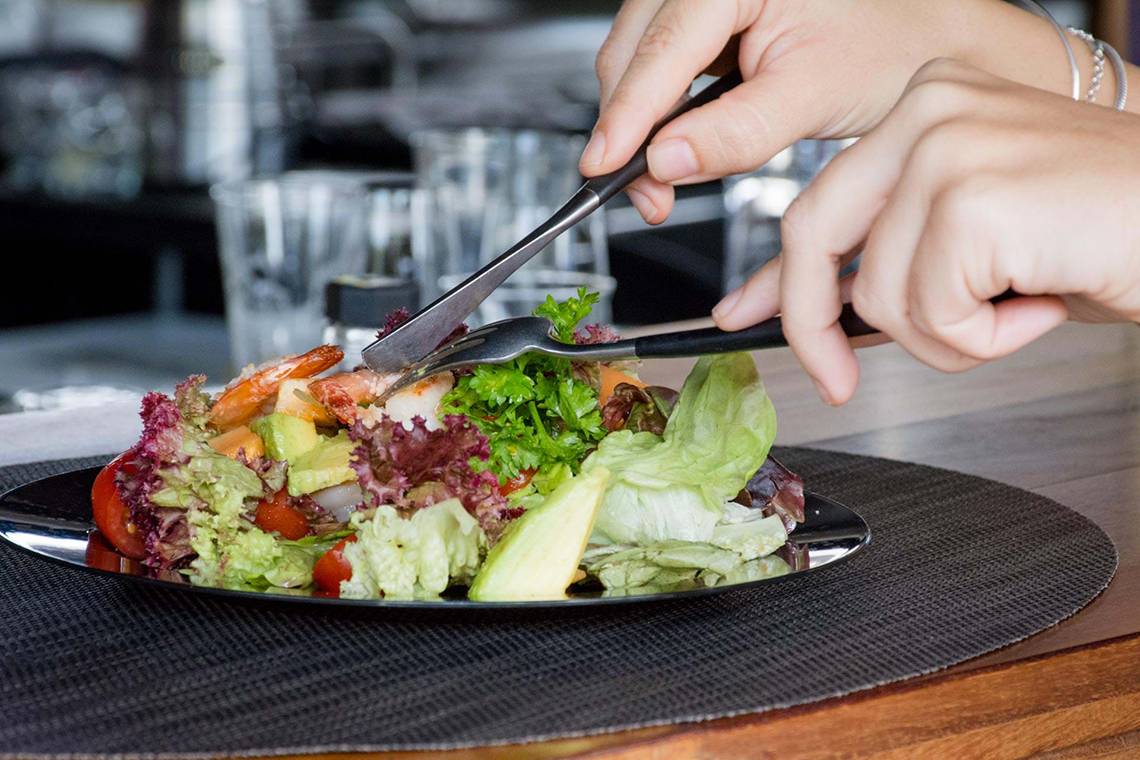 Eine Person isst Salat mit Garnelen auf einem Teller im Bohemia Suites & Spa.