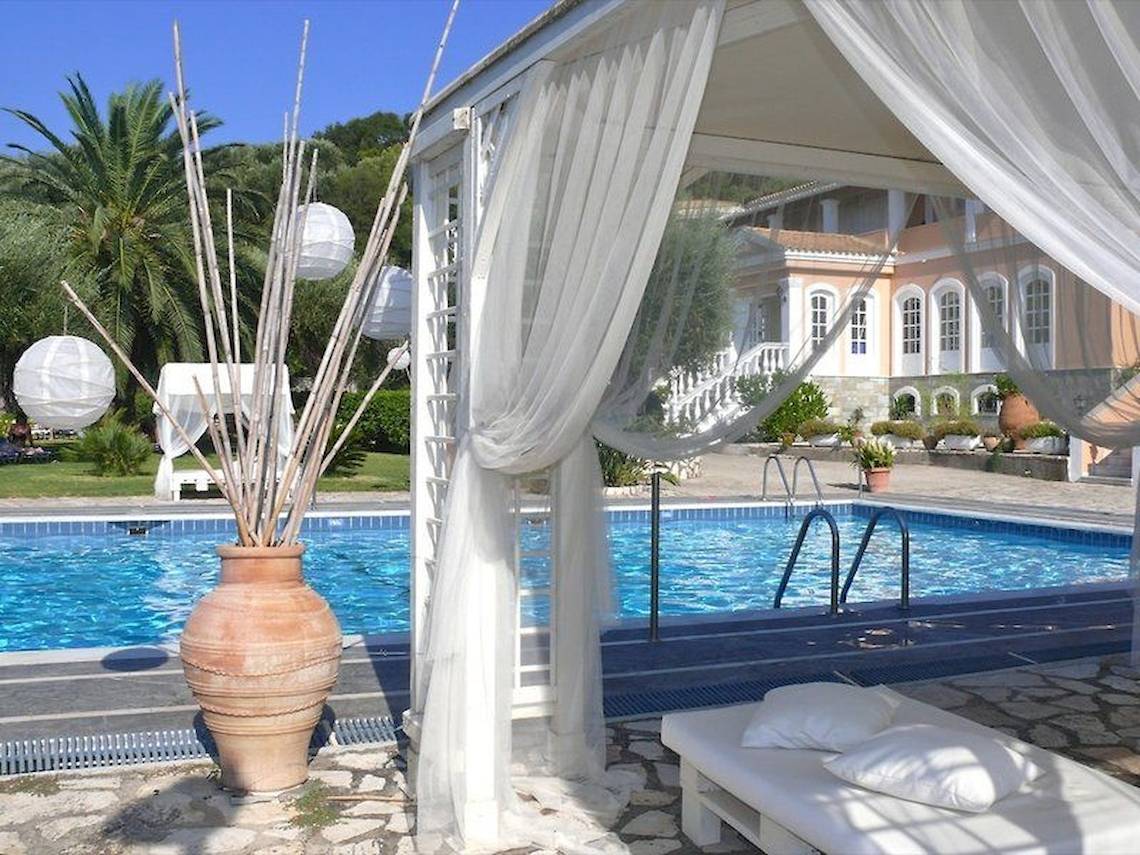 Poolbereich des Nefeli Hotels mit weißem Baldachin, einem großen braunen Krug und Blick auf das Schwimmbecken.