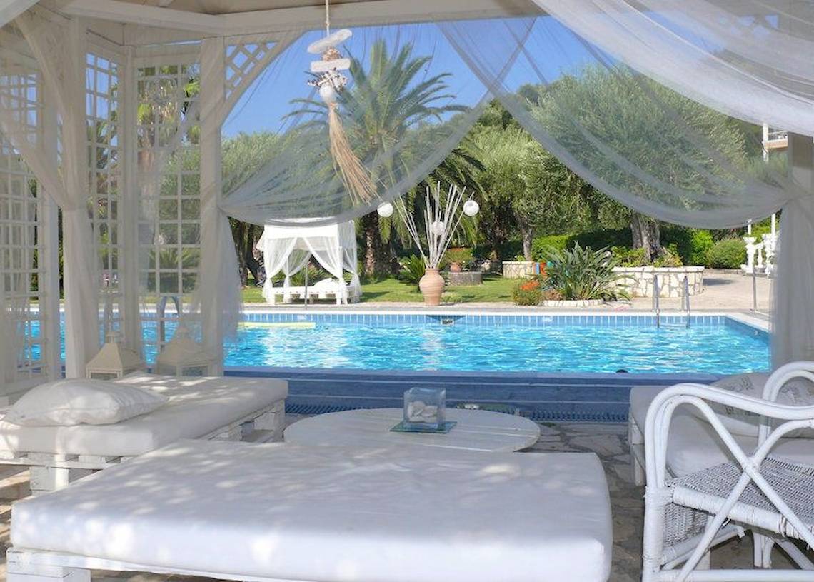 Pool-Loungebereich im Nefeli Hotel mit weißen Möbeln und Vorhängen.
