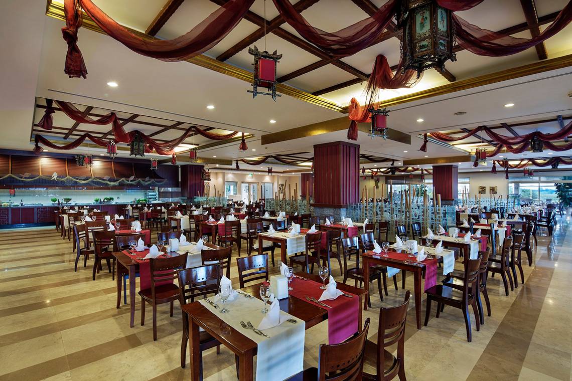 Innenansicht des Restaurants im Crystal Paraiso Verde Resort & Spa mit gedeckten Tischen und dekorativen Deckenlampen.