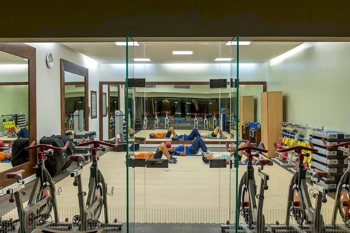 Fitnessstudio im Constance Belle Mare Plage Hotel mit Menschen, die auf Matten liegen und auf Fahrrädern trainieren.