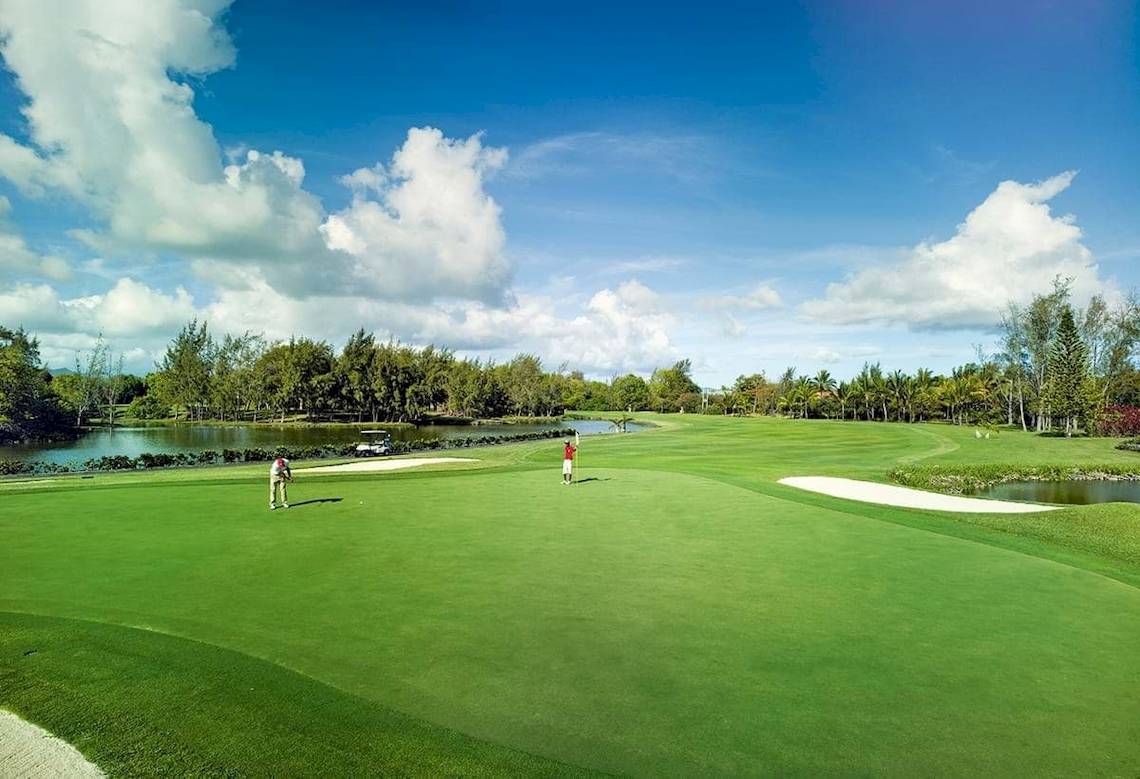 Golfplatz am Constance Belle Mare Plage Hotel mit zwei Spielern und einem See im Hintergrund.