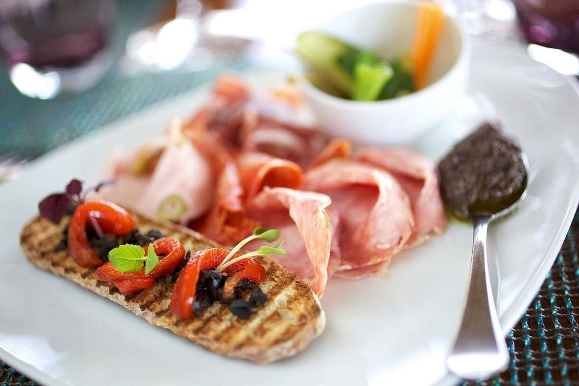Ein Teller mit geschnittenem Fleisch, Gewürzen und einem Löffel auf einem Tisch.