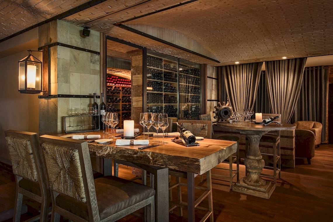 Innenansicht des Weinkellers im Constance Belle Mare Plage Hotel mit Holztischen, Stühlen und Flaschen.