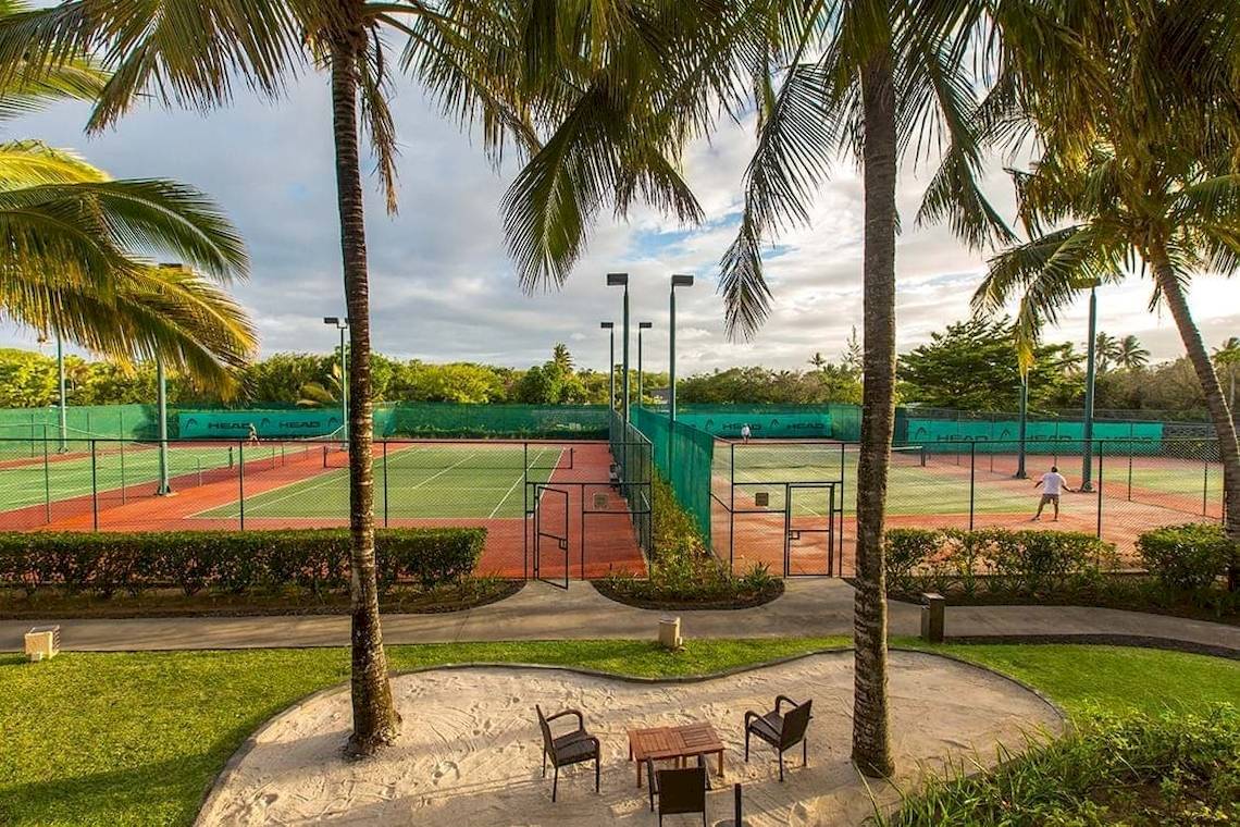 Tennisplatz im Constance Belle Mare Plage Hotel, umgeben von Palmen und Rasen.