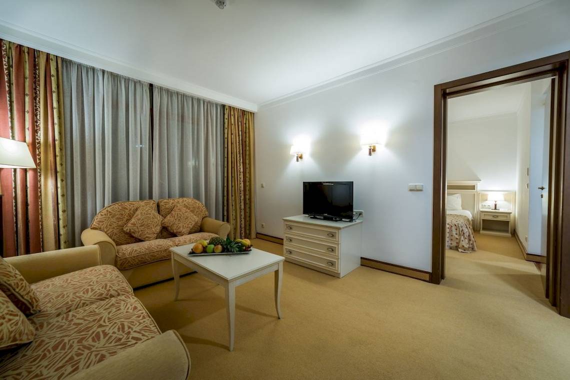 Wohnbereich im Helena Sands Hotel mit Sofas, Tisch, Fernseher und Schlafzimmerzugang.