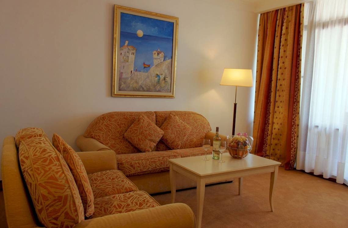 Wohnbereich des Helena Sands Hotels mit Sofas, Tisch, Lampe und Gemälde an der Wand.