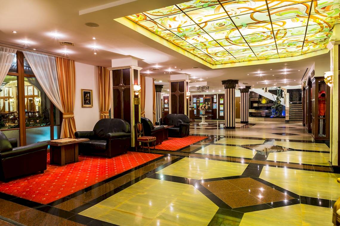 Empfangsbereich des Helena Sands Hotels mit rotem Teppich, schwarzen Ledersesseln und farbiger Glasdecke.