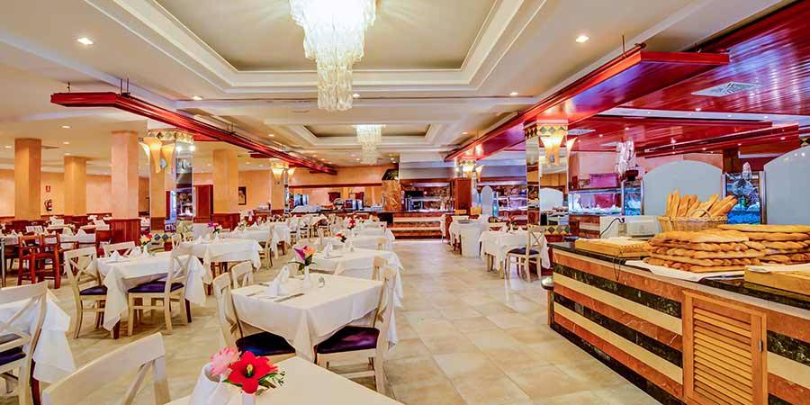 Innenansicht des Restaurants im SBH Costa Calma Beach Resort mit vielen Tischen und Stühlen, gedeckten Tischen, und einer Theke mit Brot und Backwaren.