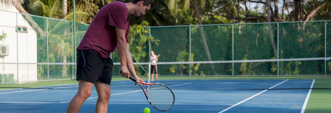Tennisspieler in einem roten T-Shirt schlägt einen Ball auf einem blauen Tennisplatz.