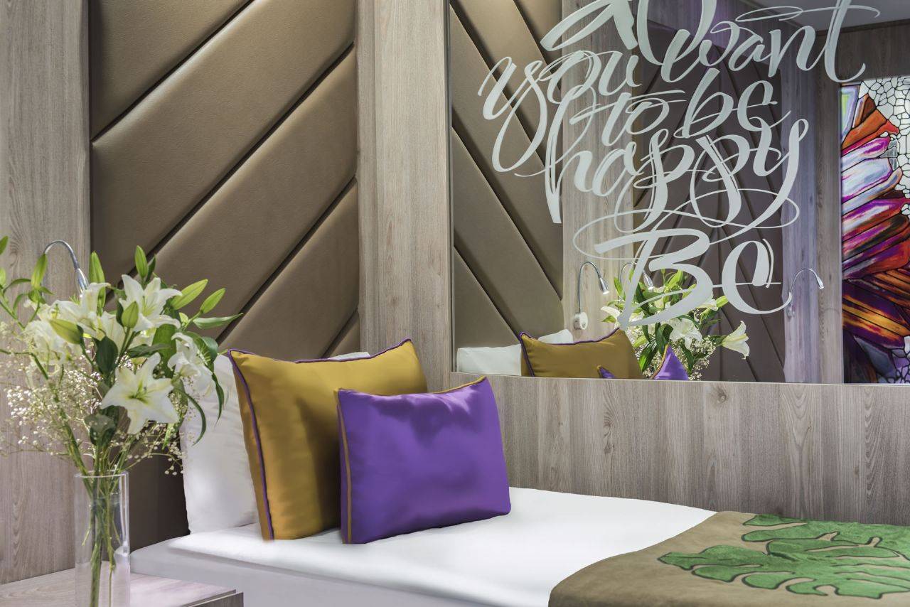Inneneinrichtung des Delphin BE Grand Resort Hotels mit Bett, Kissen und Blumenvase.