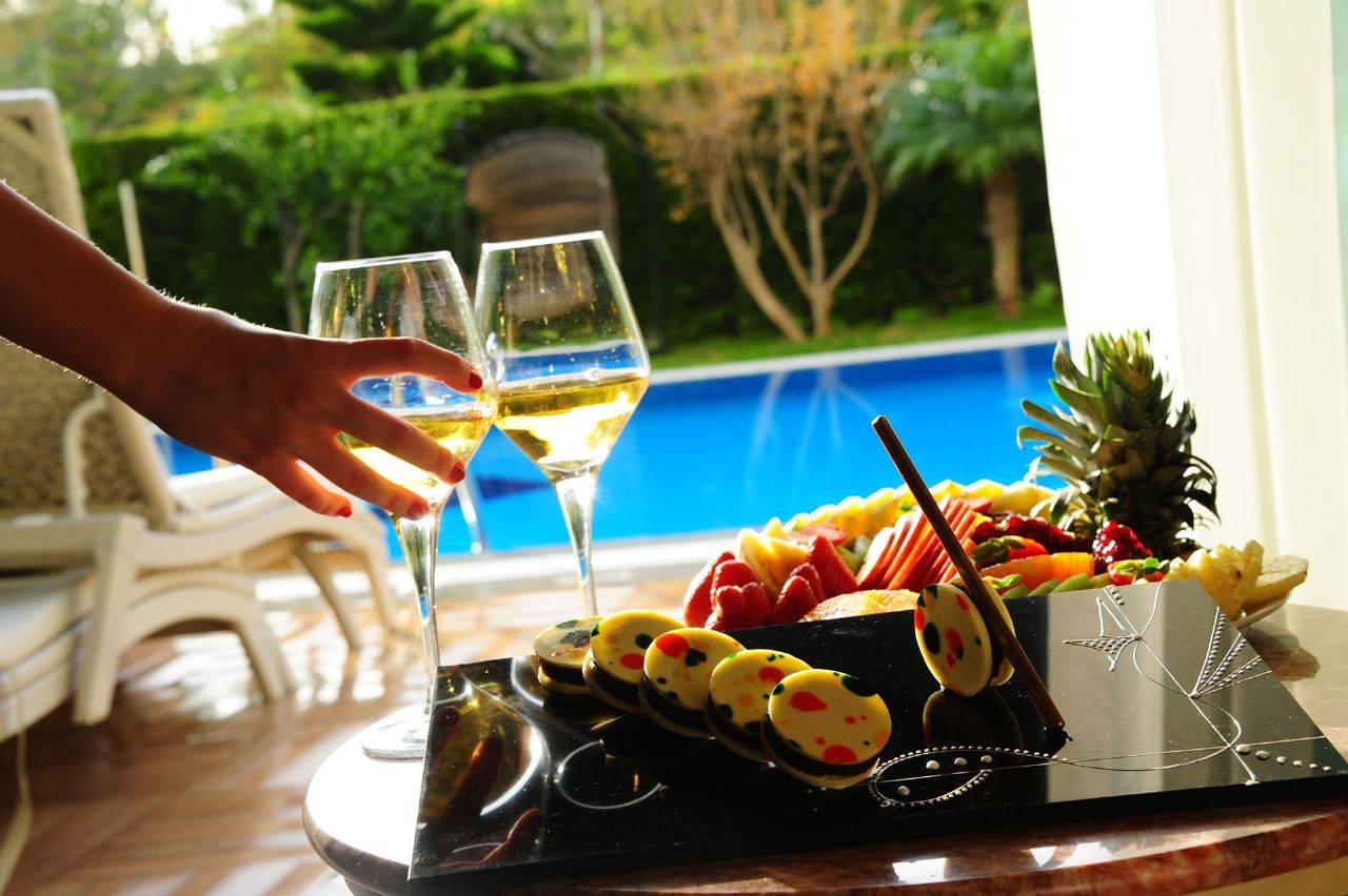 Ein Glas Weißwein und ein Teller mit buntem Obst liegt am Pool des Delphin BE Grand Resort.