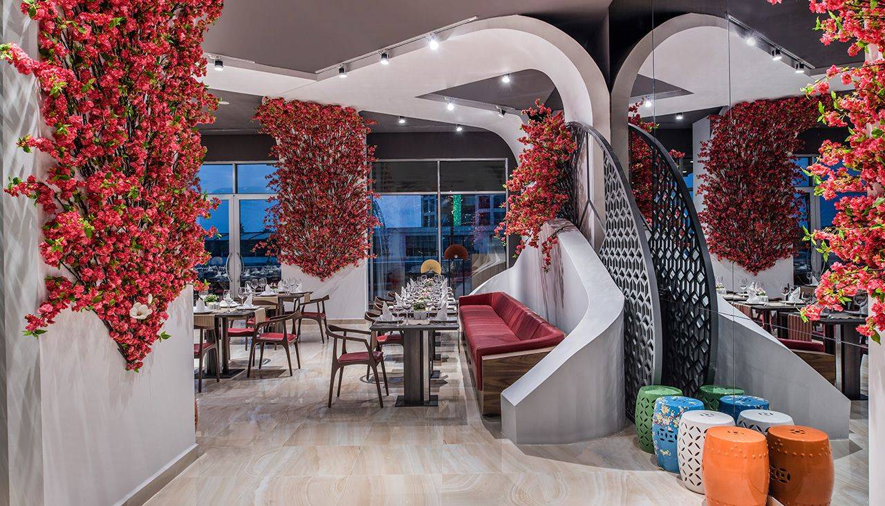 Elegantes Restaurant im Delphin BE Grand Resort, dekoriert mit leuchtend roten Blumen und stilvollen Möbeln.