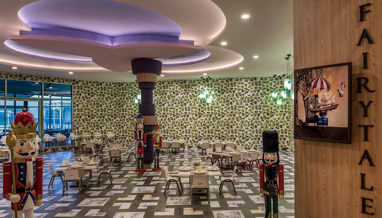 Gemütliches Restaurant im Delphin BE Grand Resort mit buntem Dekor und festlich gedeckten Tischen.