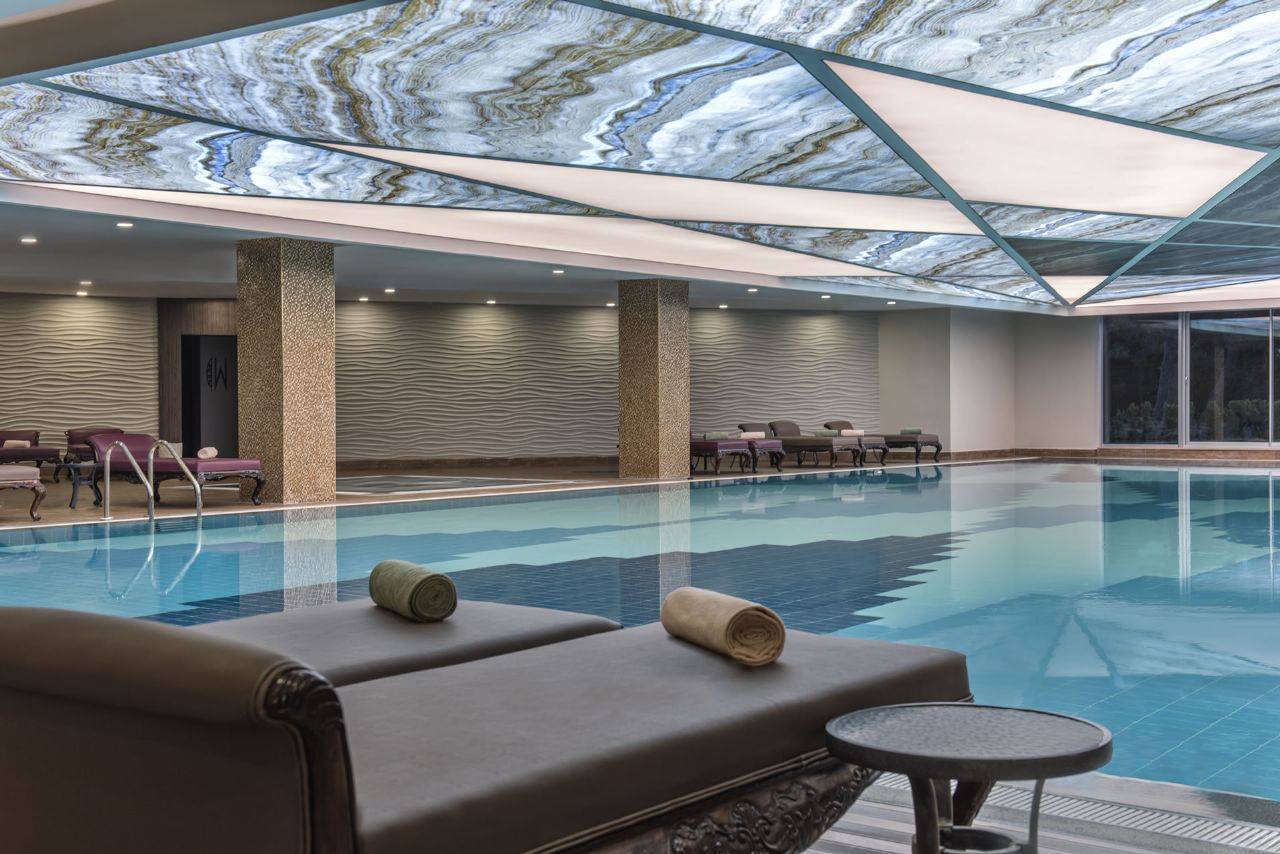Innenansicht des Delphin BE Grand Resort mit einem Pool und luxuriösen Liegen.